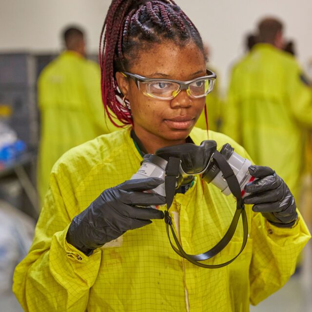 Yanique Bradford wears a yellow protective suit and prepares to put on a mask.